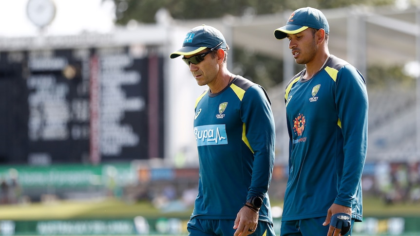 Australia men's cricket coach Justin Langer and player Usman Khawaja walk around Manuka Oval in their warm-up gear.