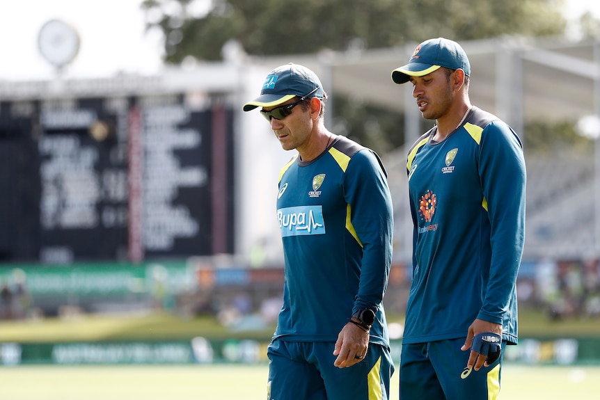 Australia men's cricket coach Justin Langer and player Usman Khawaja walk around Manuka Oval in their warm-up gear.