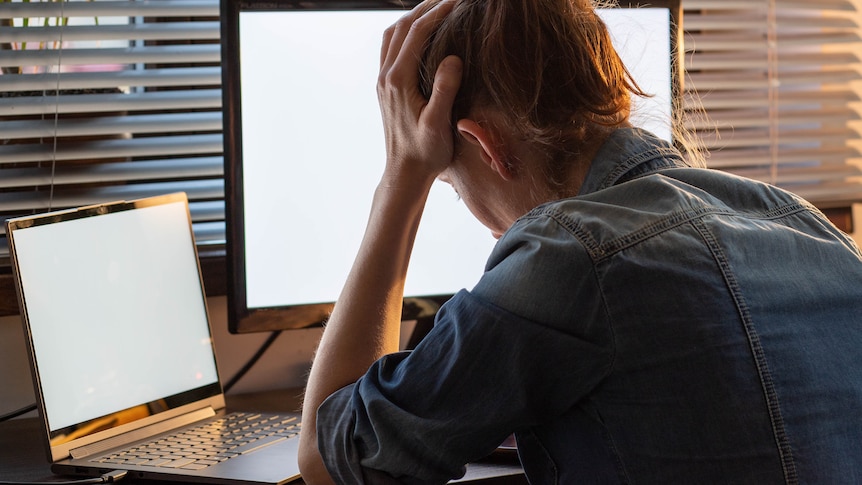 Woman holding her head in hands at work in a story about taking domestic violence leave from work.