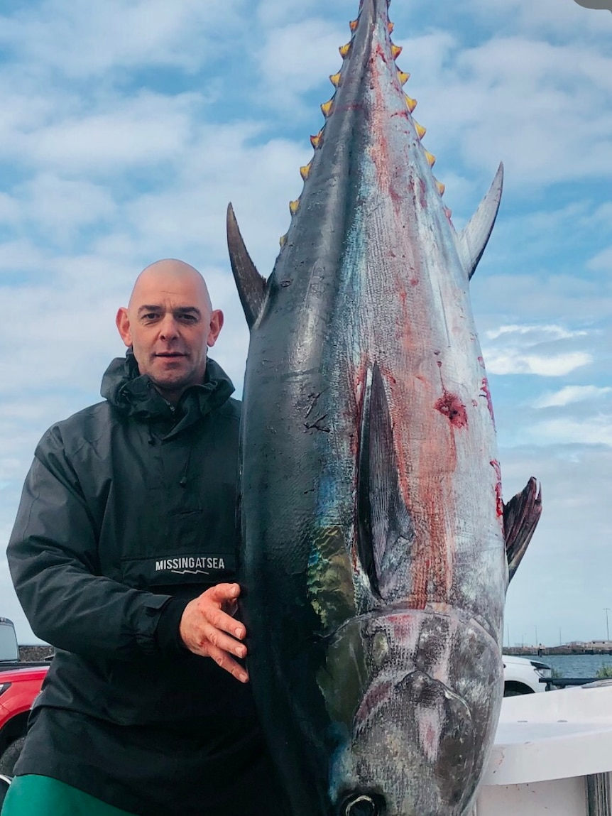 Mat Nash, a bald white man, is standing next to a giant tuna