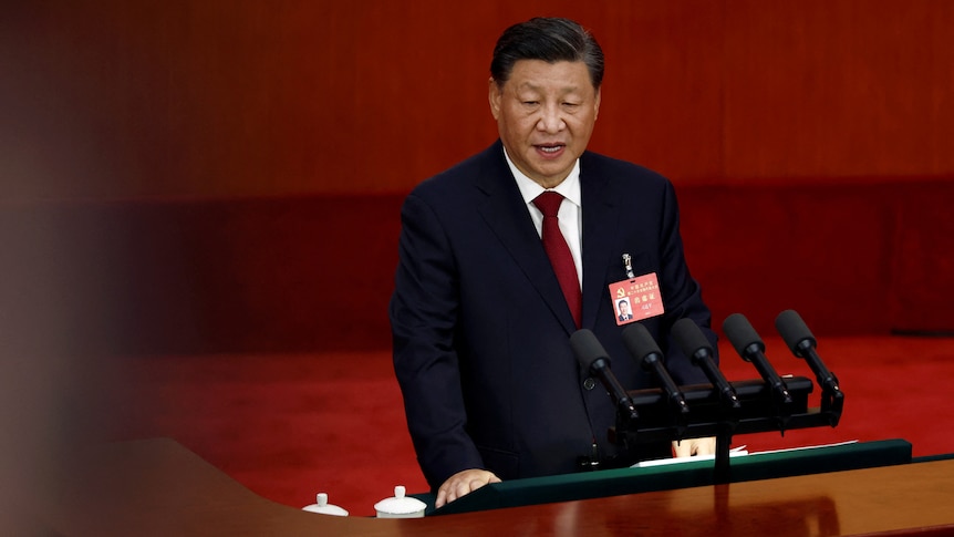 Xi Jinping speaks on a podium in front of a red background.