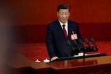 Xi Jinping speaks on a podium in front of a red background.