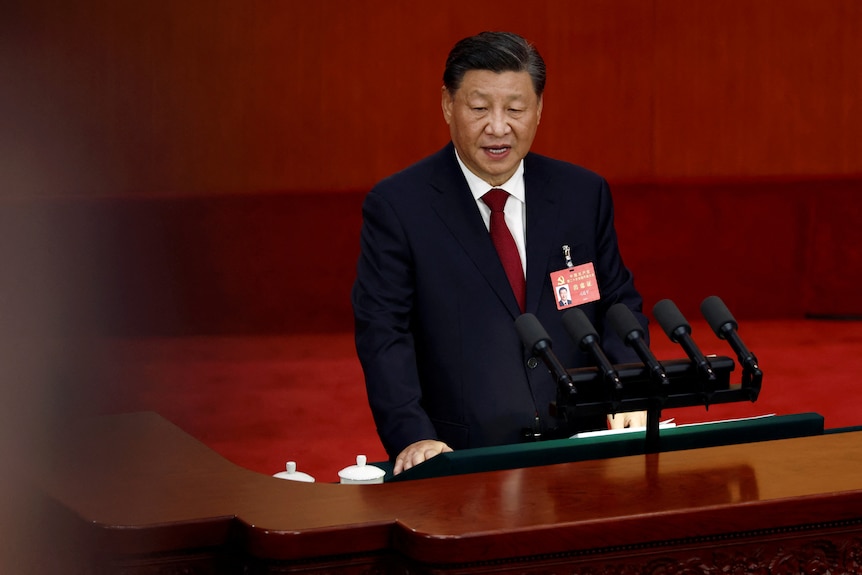 Xi Jinping speaks on a podium in front of a red background.