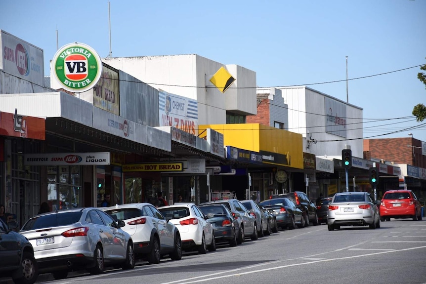 Cars are parked on the street outside the Reservoir SUPA IGA. There is a Commonwealth Bank, chemist and bakery.