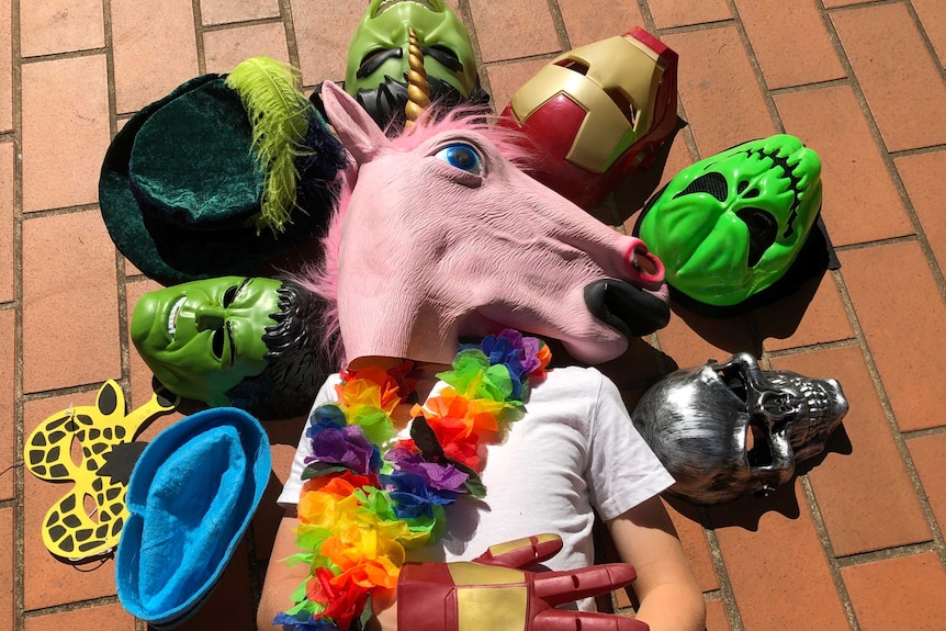 A photograph of a child wearing a unicorn head mask, surrounded by other fantasy character masks.