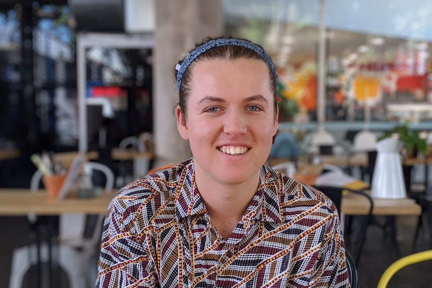 Young male wearing Indigenous print shirt smiling at camera.