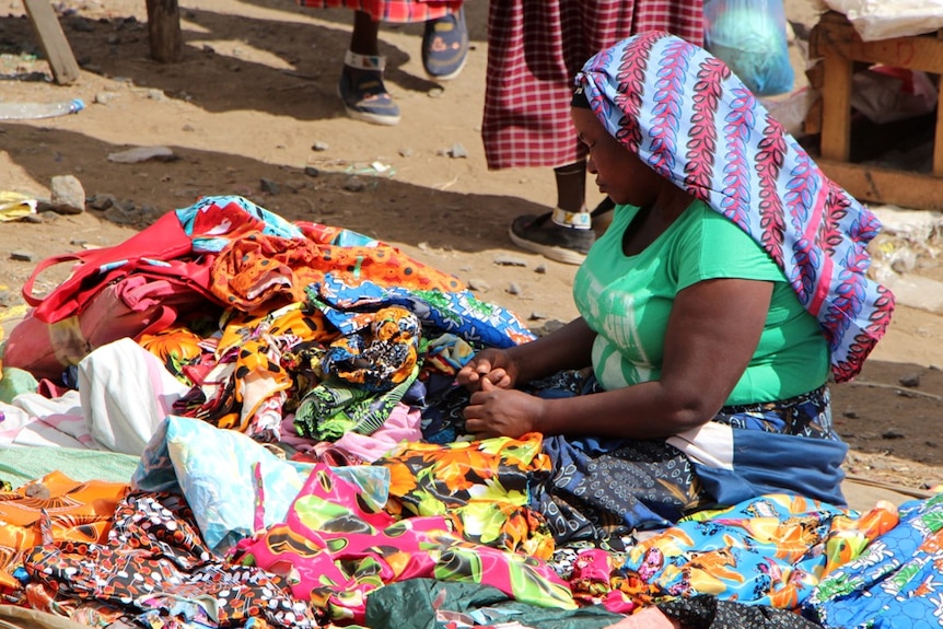 A lady sitting on the ground selling clothing