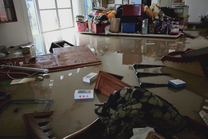 A room with cabinets and chairs and objects floating in brown water.