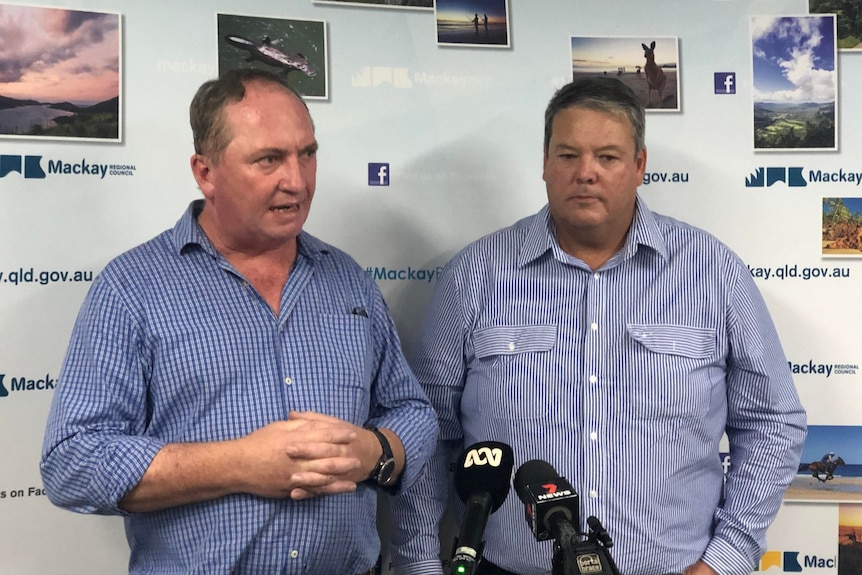 Two men stand in front of a banner that says Mackay 