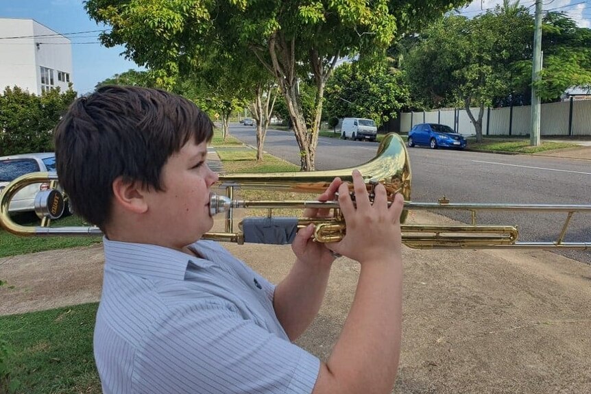 A boy playing a trombone at the end of a suburban driveway
