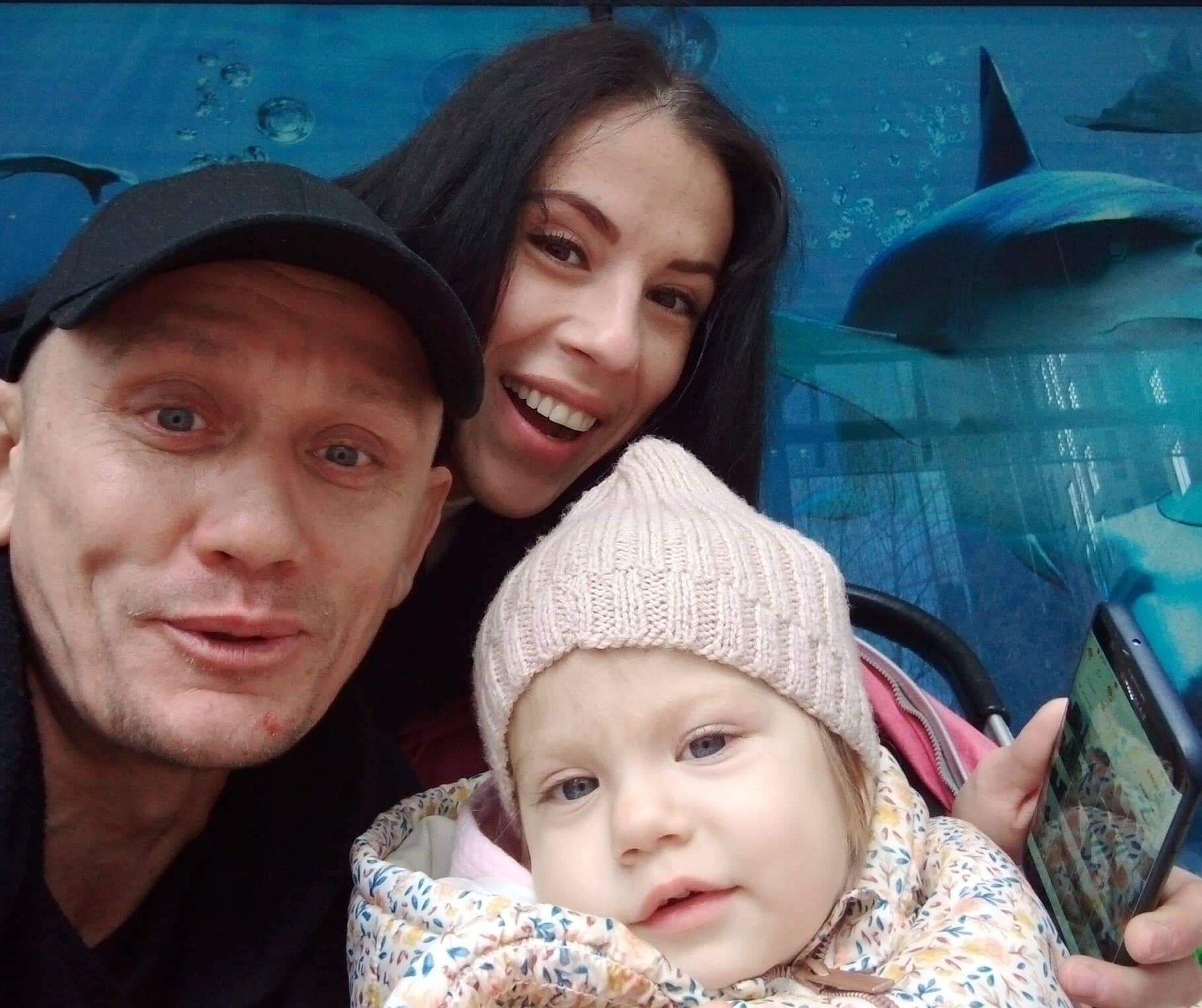 A man and a woman with a young girl smiling at the camera, aquarium is in the background