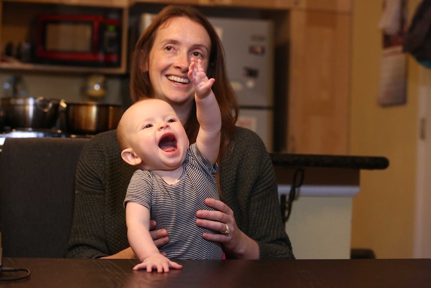 A baby smiling with her hand outstretched on her mother's lap