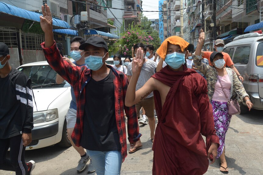 A Buddhist monk joins anti-coup protesters as they flash the three-finger salute
