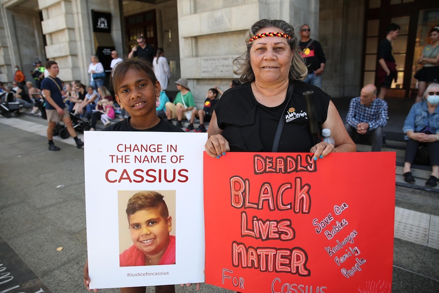 A woman and a boy hold placards while standing in front of a crowd at a rally.