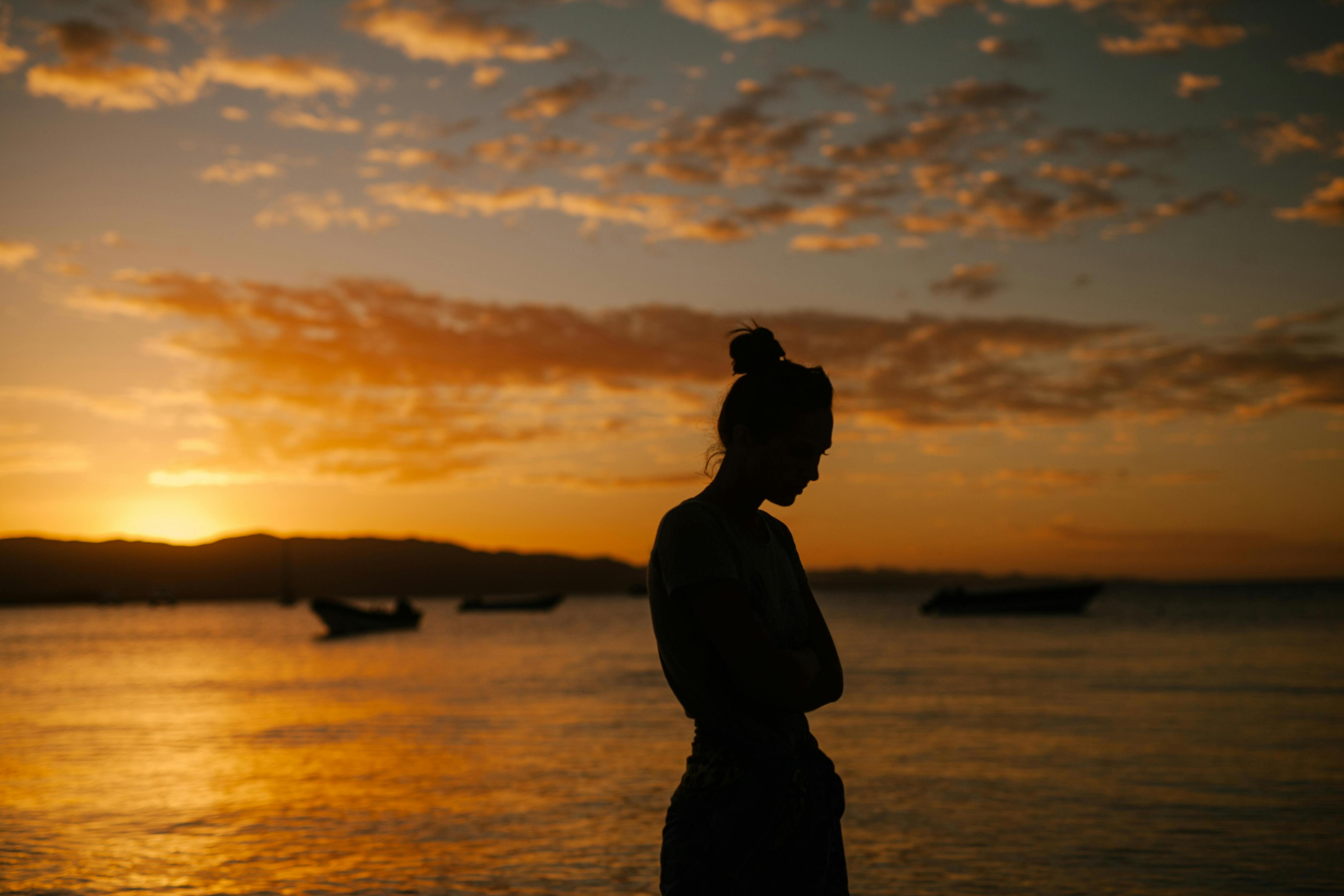 Sad woman standing on coast of sea at sunset    