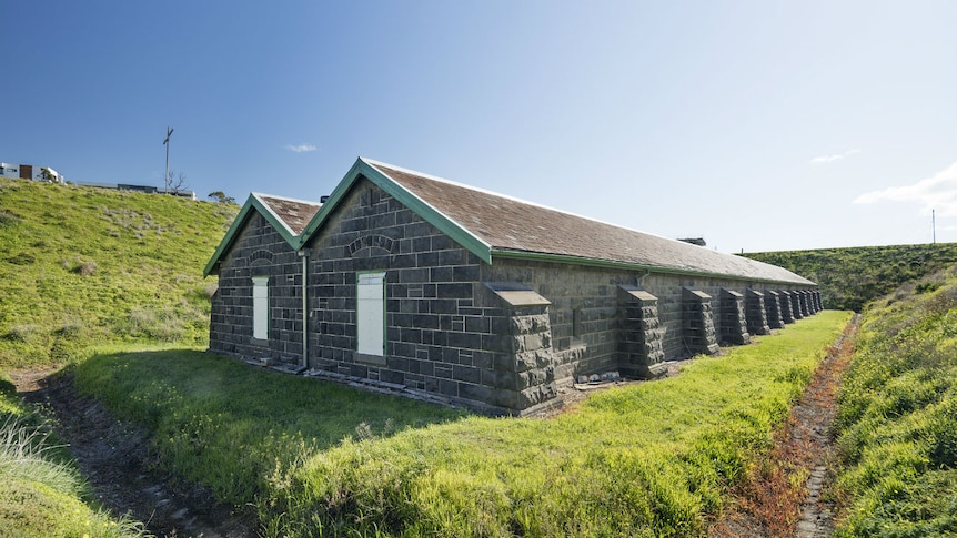 A bluestone building surrounded by green, grassy mounds under a blue sky.