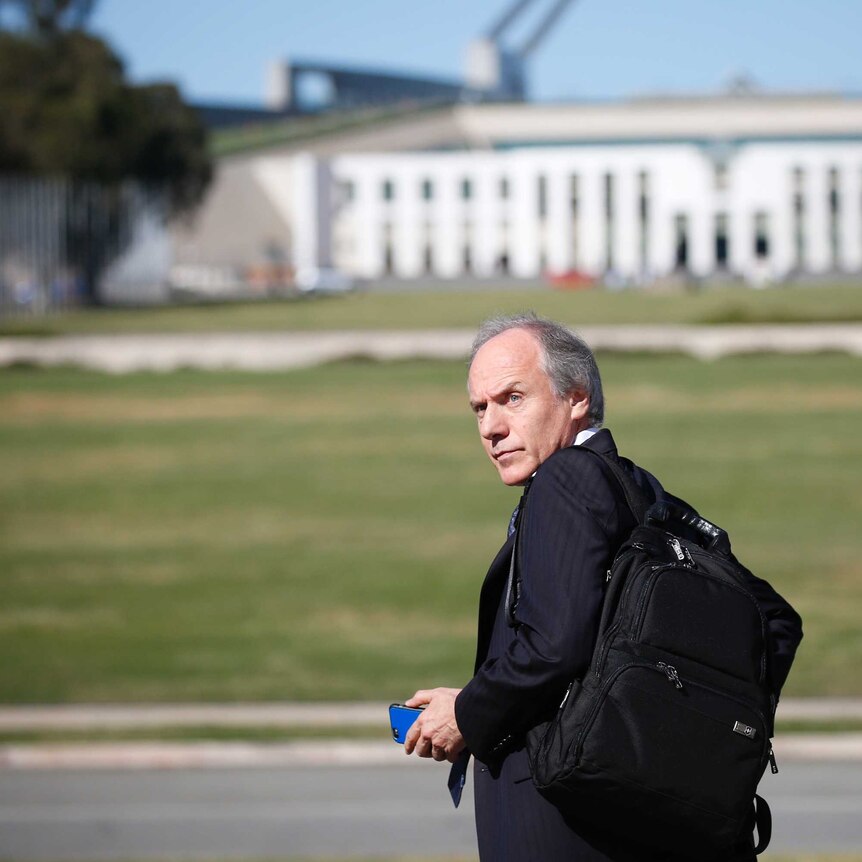 Alan Finkel walks towards the lawns of Parliament House. He is wearing a backpack and looking over his shoulder.
