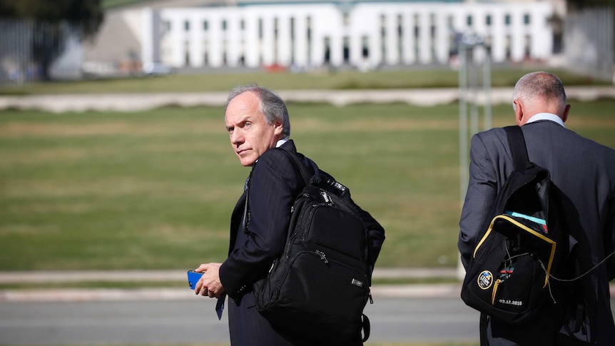 Alan Finkel walks towards the lawns of Parliament House. He is wearing a backpack and looking over his shoulder.