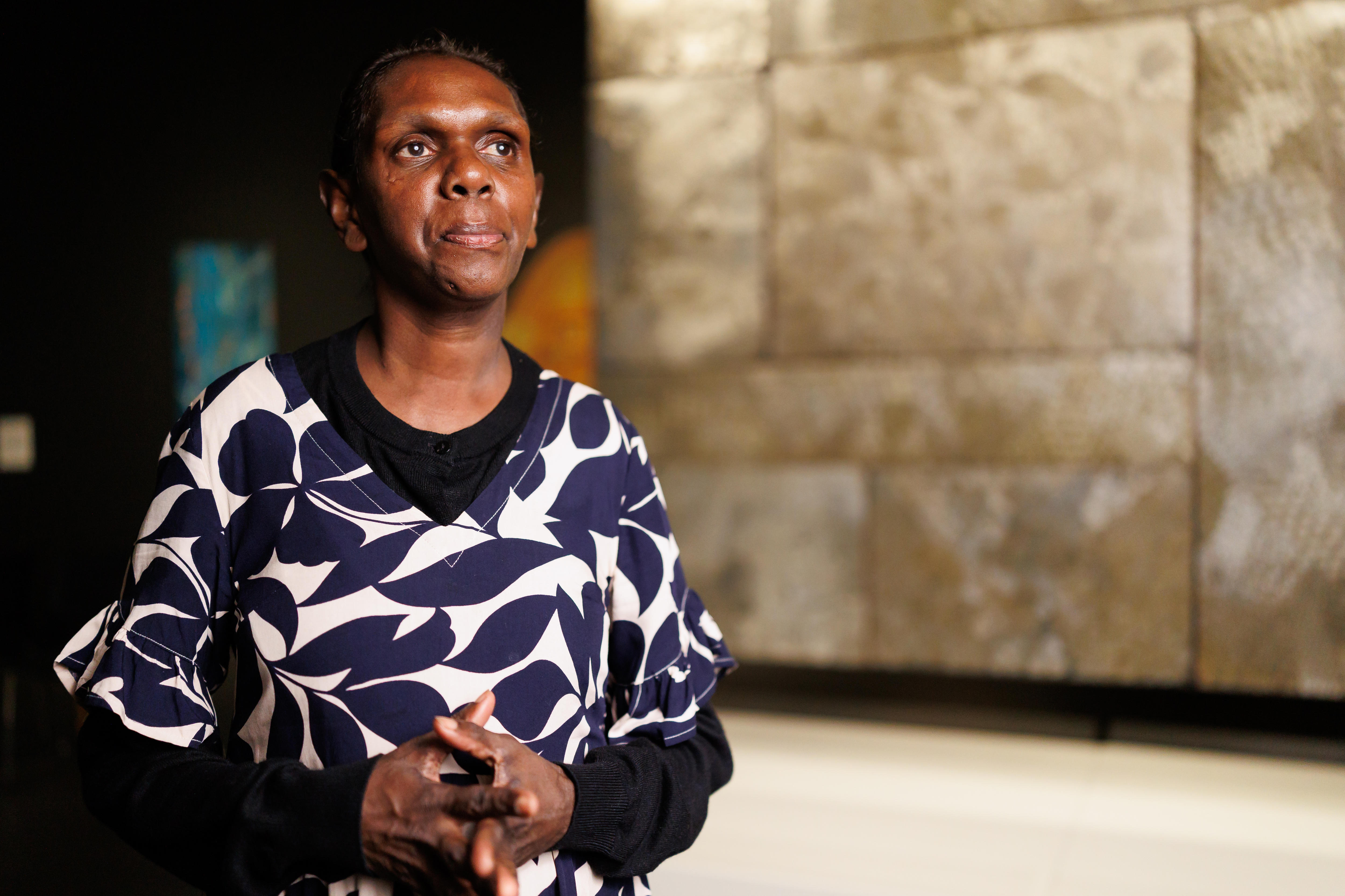 Gaypalani Waṉambi, an Indigenous woman in her late 30s, poses in front of an intricately designed etched metal art work.
