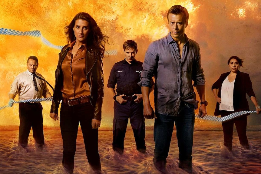 A tv promo of five actors standing in ocean water, surrounded by flames.
