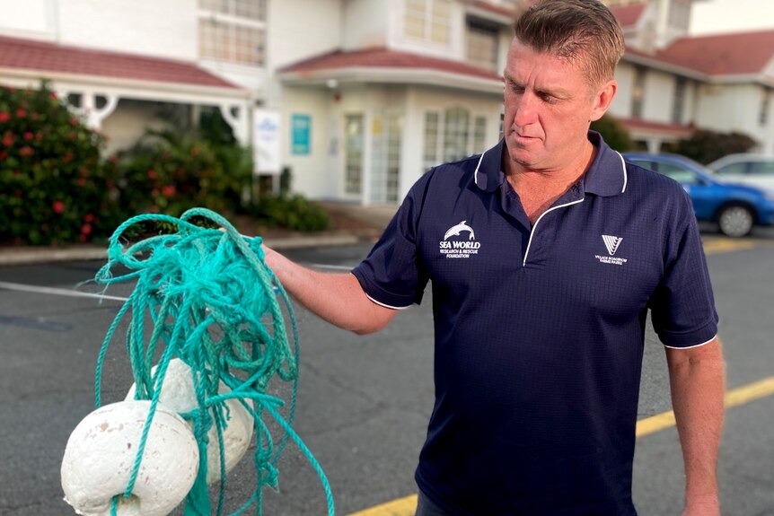 A man with a blue shirt holds an old fishing rope and buoys.