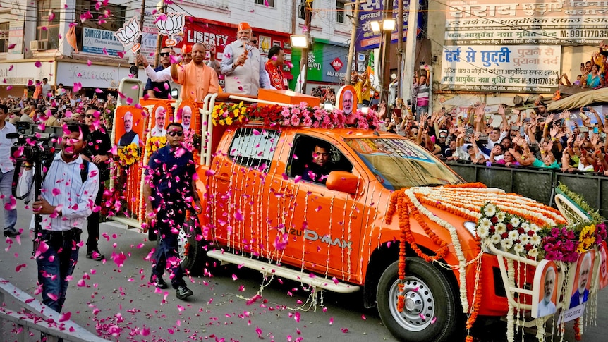 Narendra Modi rides in the back of a ute past a cheering crowd during a colourful election roadshow.