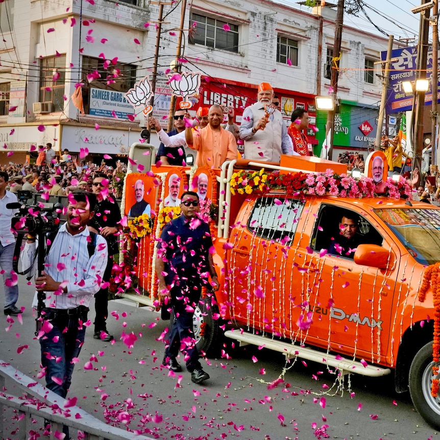 Narendra Modi rides in the back of a ute past a cheering crowd during a colourful election roadshow.