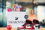 A swarovski bag full of cash and coupons, a pair of Air Jordans, a watch, a bottle of perfume and an apple. 
