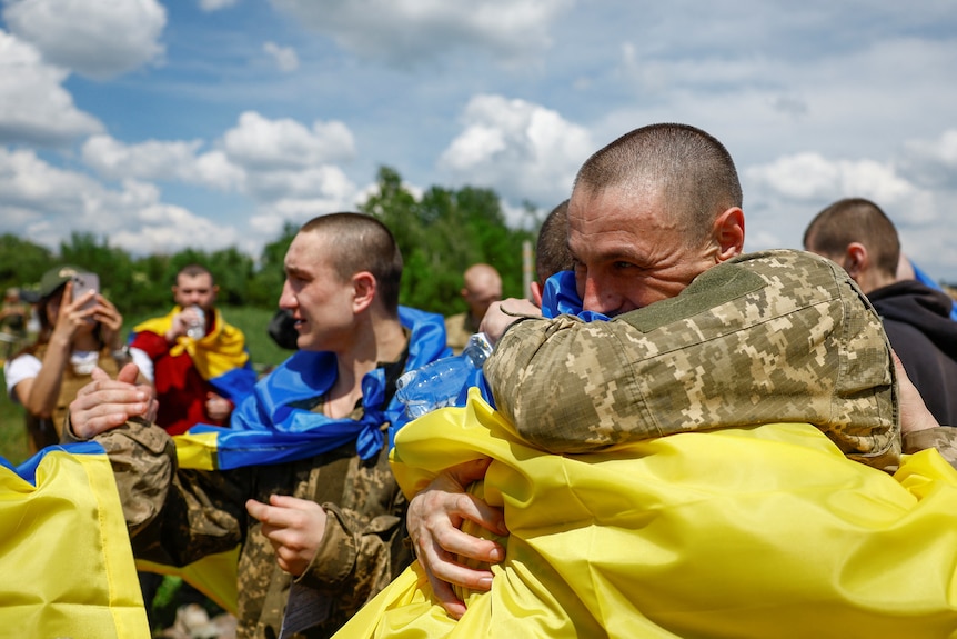 Men with shaved heads covered in Ukrainian blue and yellow flags smile and hug each other