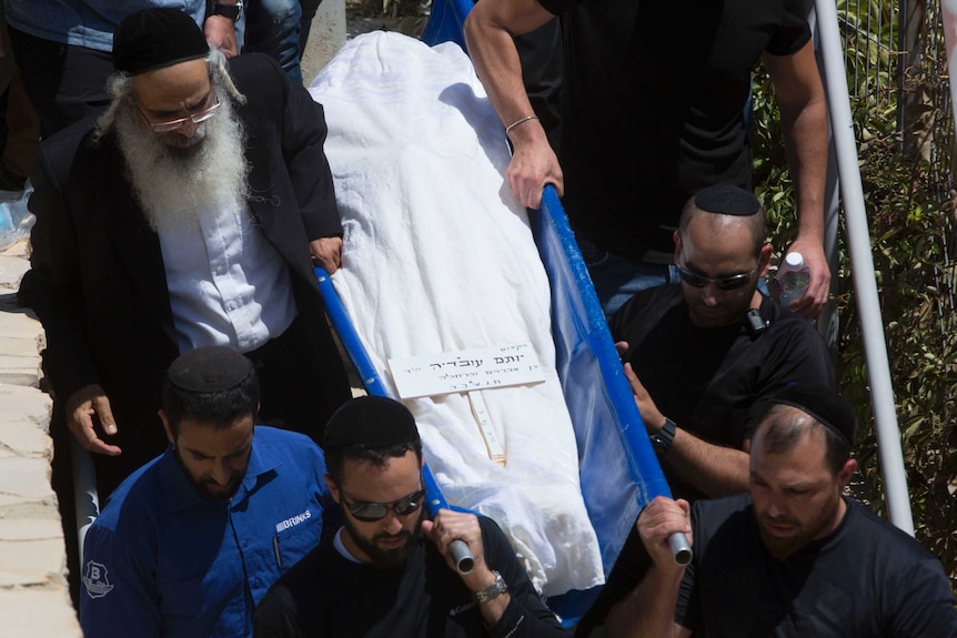 Men are seen carrying a body during a funeral procession.