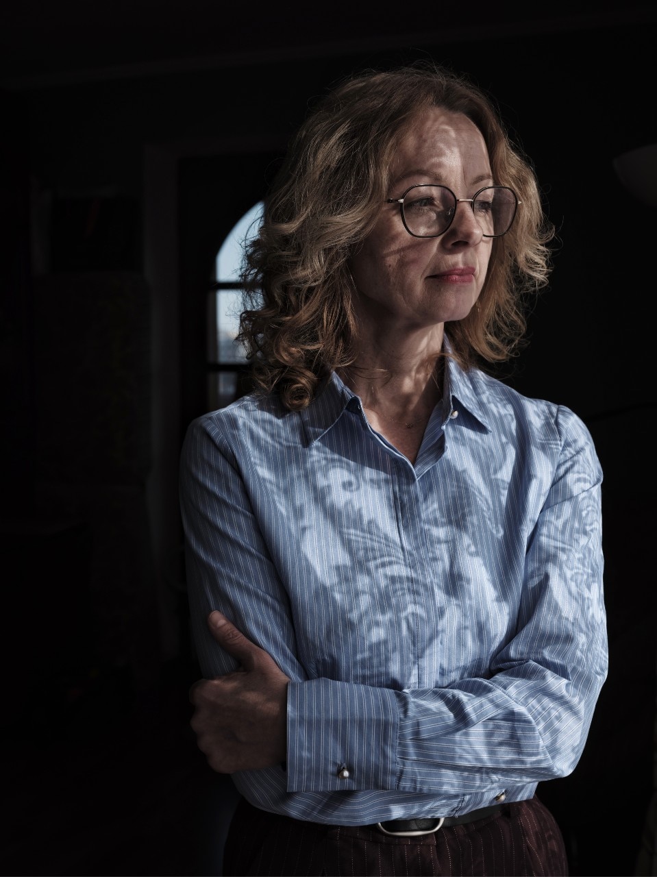 A woman looking out a window, with a neutral expression on her face.