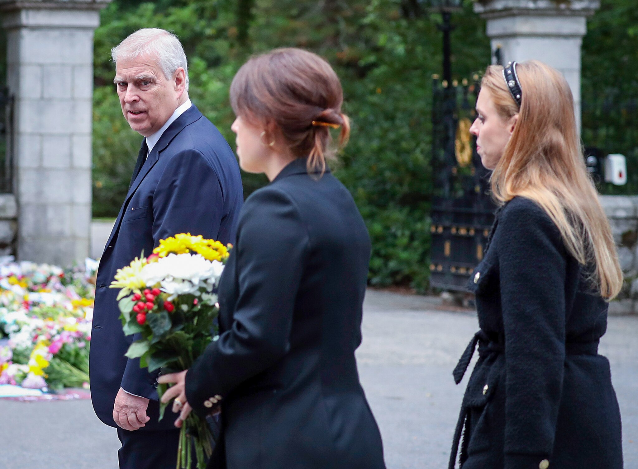 Prince Andrew walks with Eugenie and Beatrice. Eugenie is clutching a big bouquet of flowers