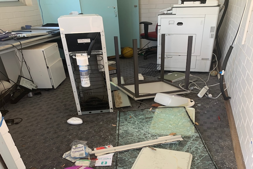 Smashed table, glass, and other office items strewn across the floor 