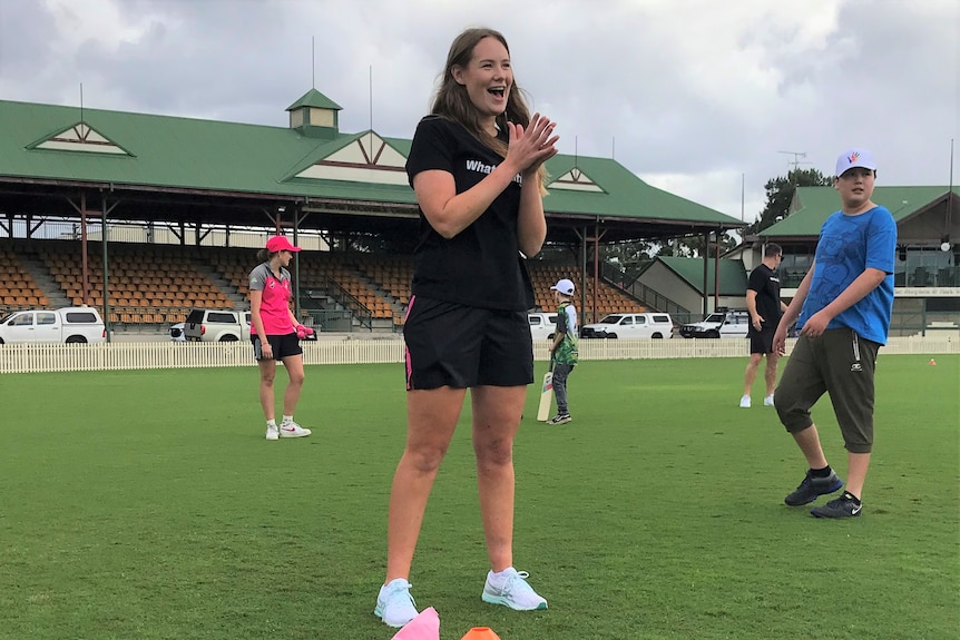 Lauren Cheatle smiles and claps while on a cricket oval.