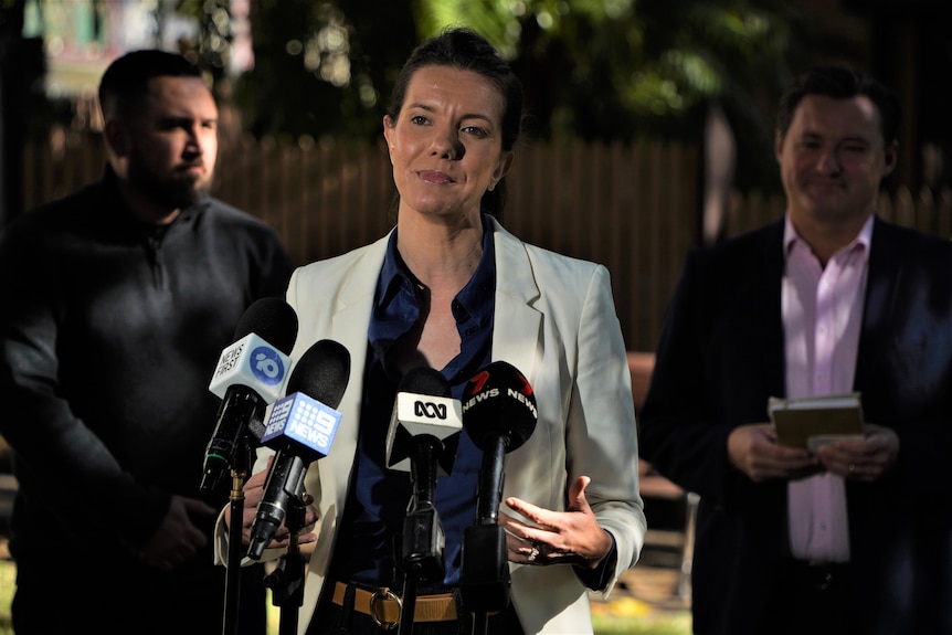 A woman at a press conference with two men behind her