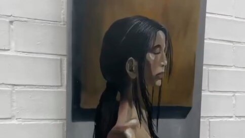 An oil painting of a side profile of dark haired young woman hanging on a white brick wall