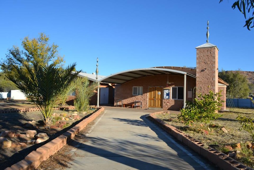 A concrete path leads to a brick building with a minaret.