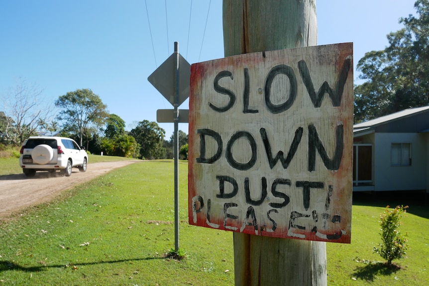 A sign next to a dirt road reads: SLOW DOWN PLEASE DUST