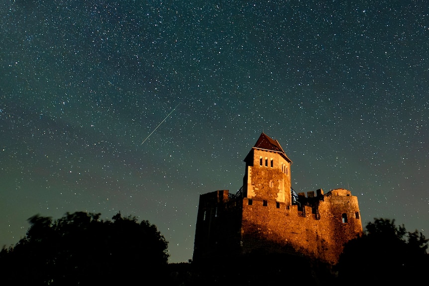 A meteor in the night sky above a castle
