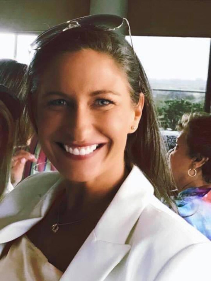 A smiling woman with long hair and a white jacket. 