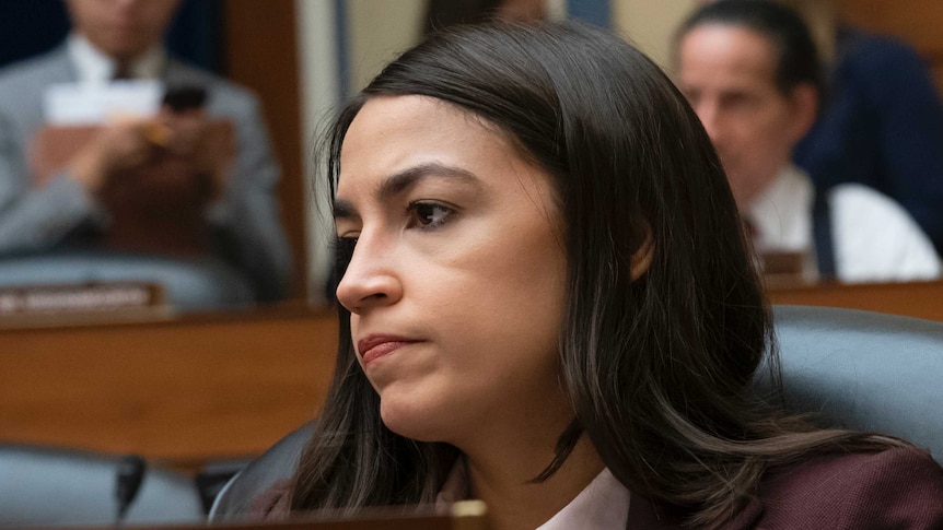 Alexandria Ocasio-Cortez, sitting at her spot in the house, looking disappointed