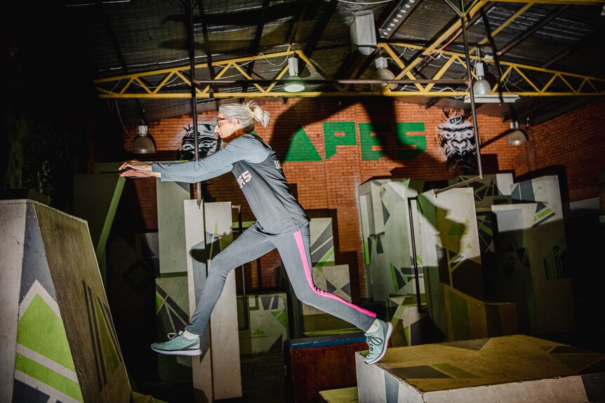 Penny Szetkuti leaps from one box to another in a gym.