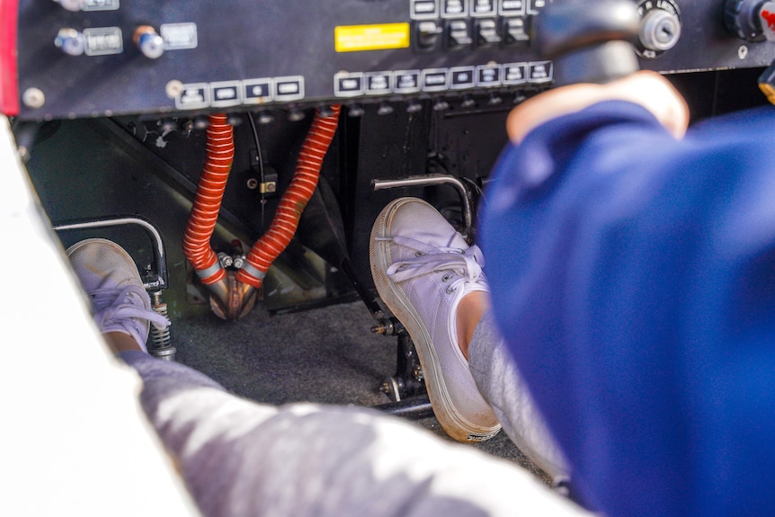 Two small feet in white shoes barely reach the pedals in a plane cockpit.