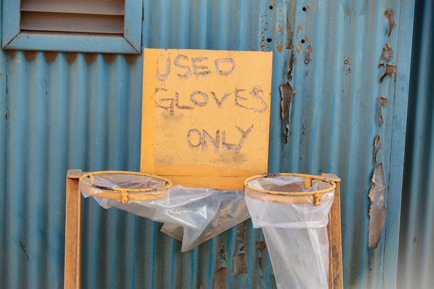 Words scratched into a metal sign above a plastic bin which reads "Used Gloves Only"