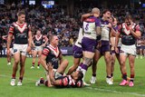 Melbourne Storm players jump, shout and celebrate a try as Roosters defenders look dejected. 