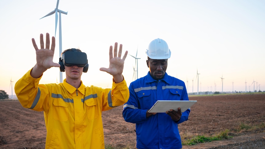 A man stands in front of wind turbines using googles