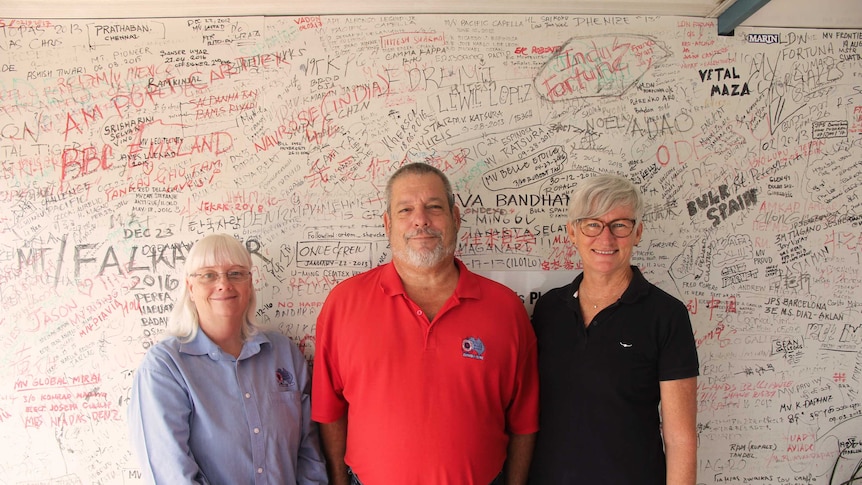 Three people in front of a wall with lots of writing on it