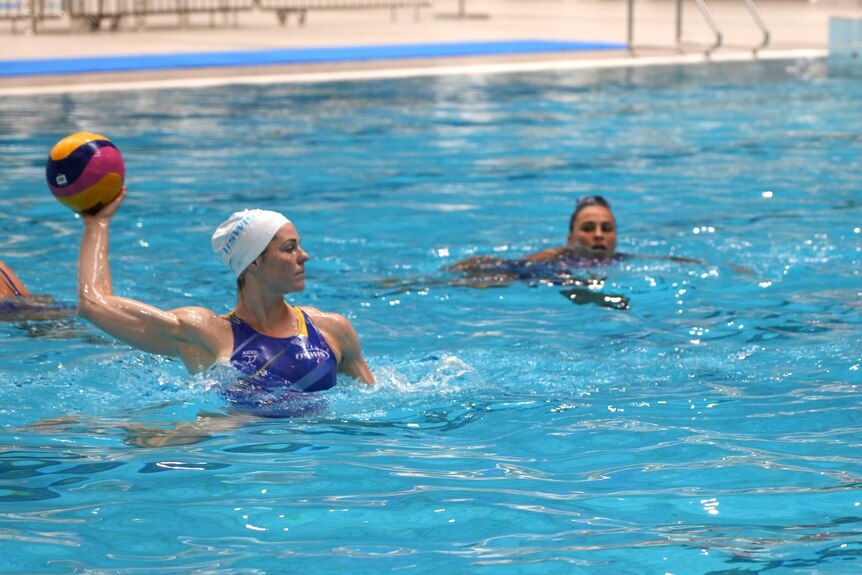 A female water polo player is training, she holds the ball in one raised arm, poised to throw
