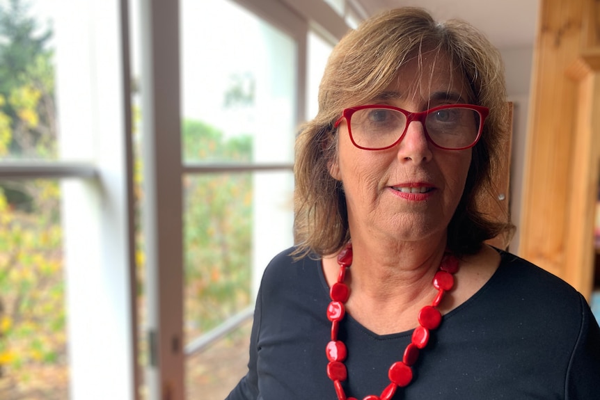 Sarah Russell wearing red glasses and a necklace, looking at the camera in a portrait taken indoors.