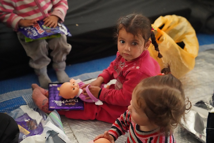 Children sit on the floor playing with dolls.